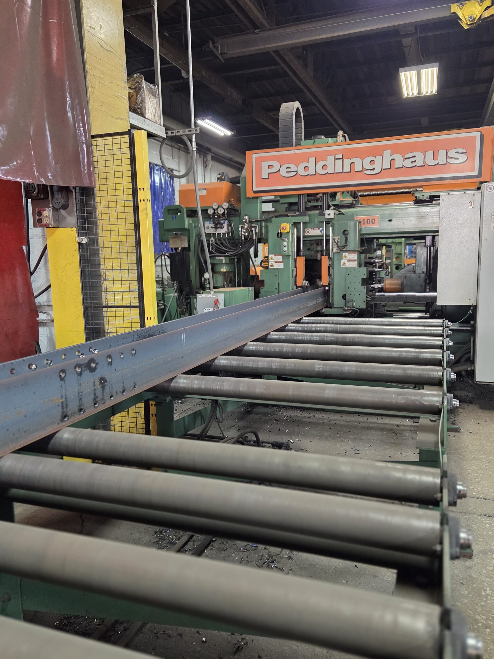 Large structural steel beams on a conveyor line at Lockport Steel's production facility.